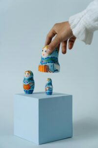 Hand placing a vibrant Russian nesting doll on a blue cube, showcasing traditional art.